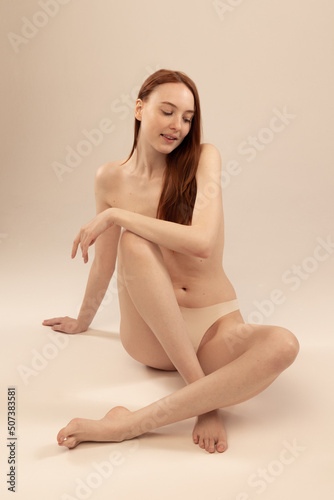 Portrait of beautiful tender woman sitting on floor isolated over grey studio background. Self-acceptance