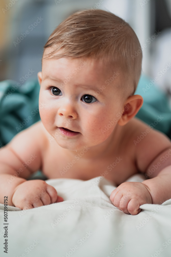 cute little naked 6 month old baby lying on stomach and looking up in prone position after bathing wrapped in turquoise towel at home cute little naked 6 month old baby lying on stomach and looking up in prone position after bathing wrapped in turquoise towel at home