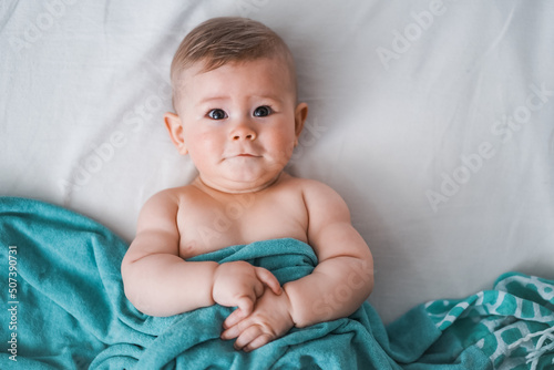 Top view of cute little naked 6 month old baby wrapped in turquoise towel and laughs at camera on a white background 