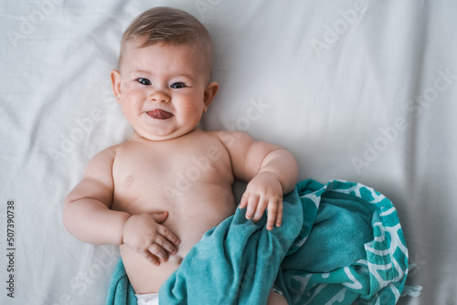 Top view of happy little cheeky 6 month old baby wrapped naked in turquoise towel and smiles & sticks tongue out at camera on a white background
 photo