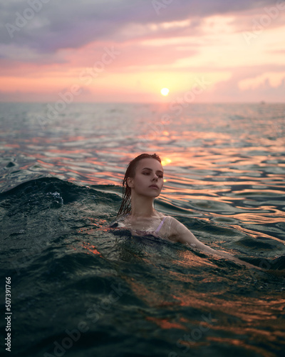 Young woman is swimming in the sea before sunset.