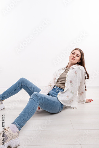 A girl with long hair in jeans and a shirt is sitting on the floor