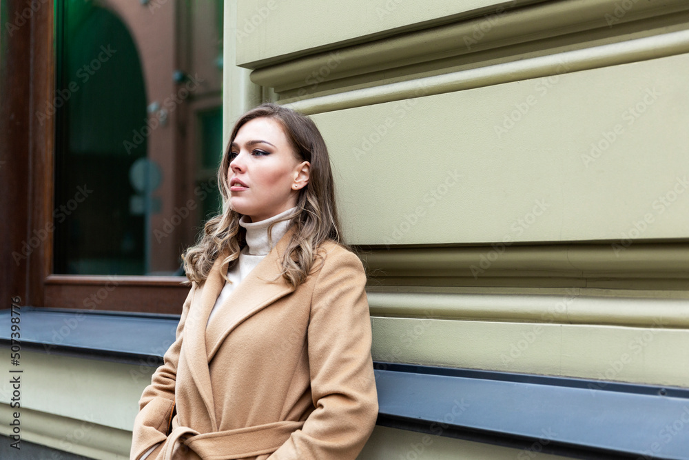 A pensive young woman stands on the street in the city. Beautiful young blonde in a beige coat. Stress, depression and loneliness. A pensive young woman stands on the street in the city. Beautiful young blonde in a beige coat. Stress, depression and loneliness.
