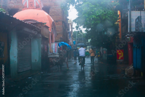 Fototapeta Naklejka Na Ścianę i Meble -  Howrah, West Bengal, India - 17th August 2019 : People walking at the wet street with umbrellas, monsoon image shot through car windshield.