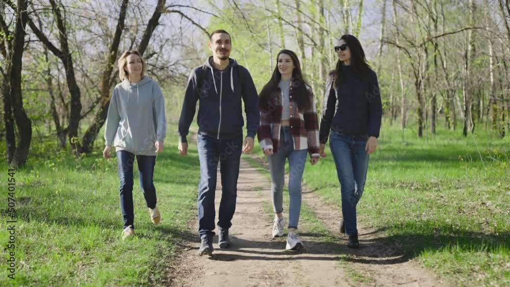 Four friends are walking in the park in nature. The women and the man are having a carefree conversation. Four friends are walking in the park in nature. The women and the man are having a carefree conversation.