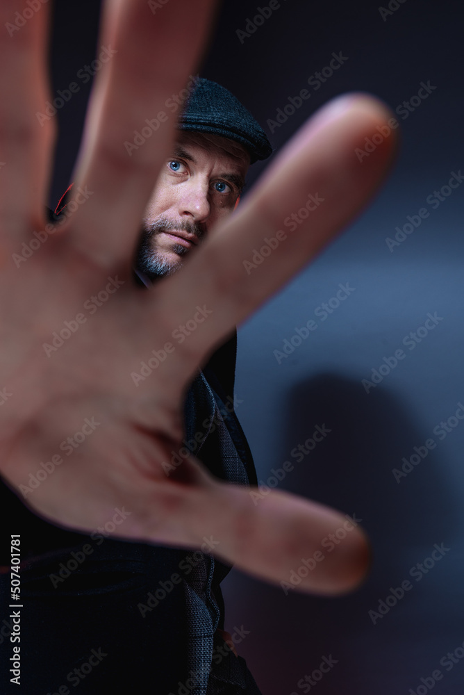 A man in a classic suit, coat and cap. A look through the fingers.