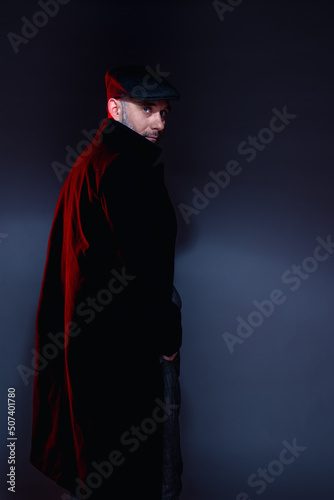 A man in a classic suit, coat and cap. Standing and looking ahead.