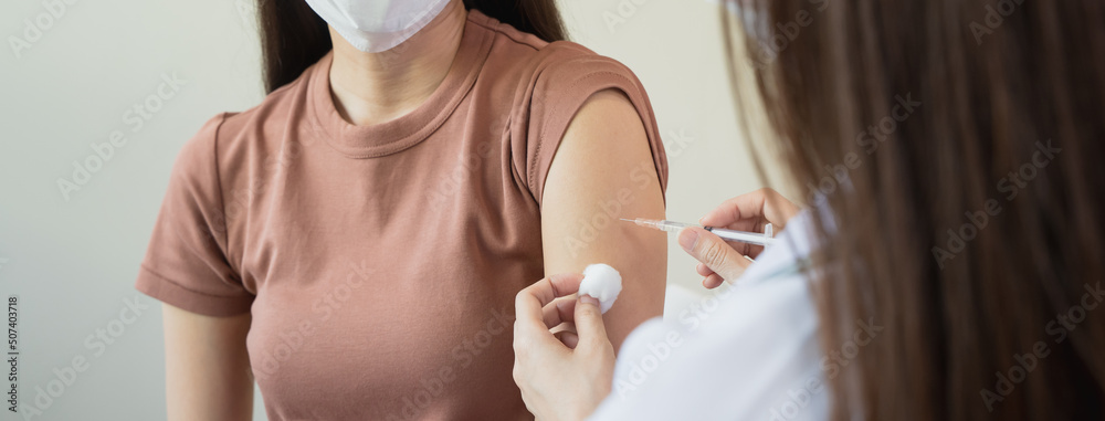 People getting a vaccination to prevent pandemic concept. Woman in medical face mask  receiving a dose of immunization coronavirus vaccine from a nurse at the medical center hospital - obrazy, fototapety, plakaty 