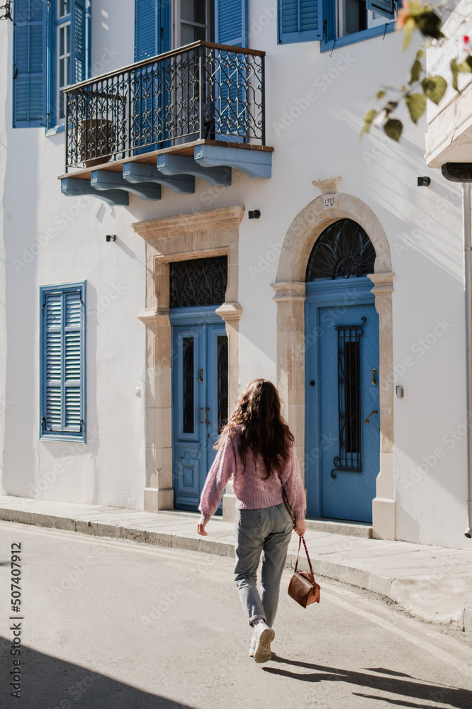 Woman is walking near beautiful building with blue doors and windows in Cyprus