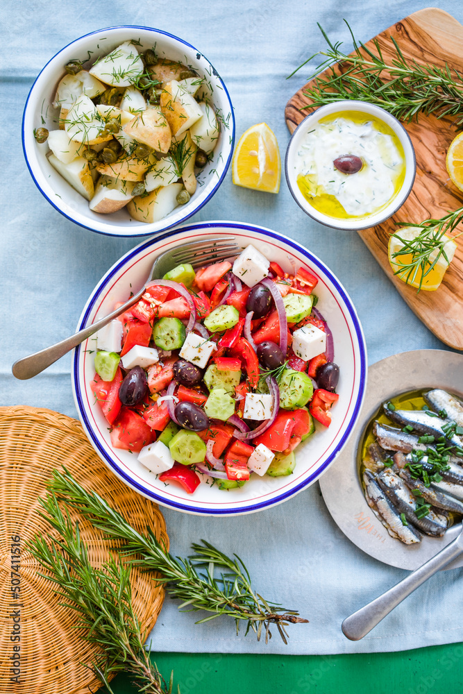 Greek food table scene, top view . Variety of items including greece salad, cucumber dip Tzatziki, Anchovy fillets, lemon potatoes.