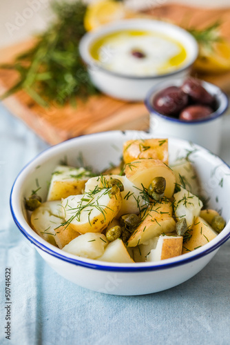 Potato salad with dill and olives in a  bowl on a blue  background.  Healthy food, vegan and lean recipes.