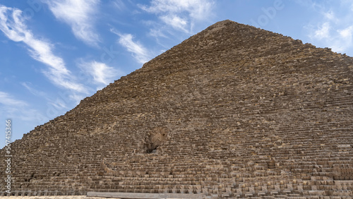 The Great Pyramid of Cheops on a background of blue sky and clouds. The masonry of the walls and the opening- the entrance inside are visible. Egypt. Giza