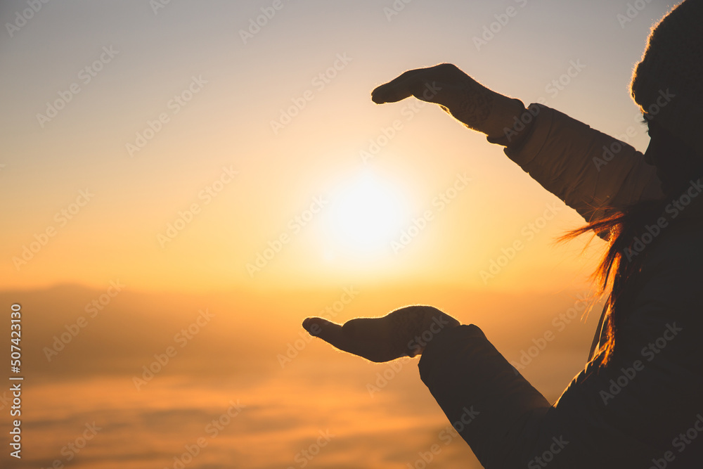 Honest woman silhouette holding sun on mountain peak at sunrise with warm background.