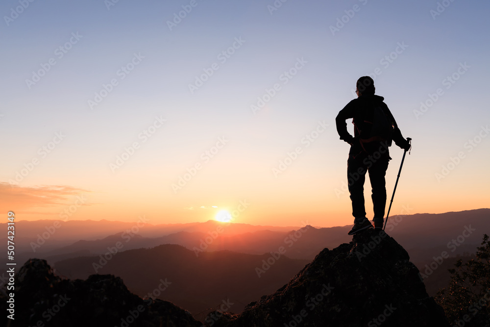 Silhouette of hiker standing on top of hill and enjoying sunrise over the valley.   Ambition and success concept