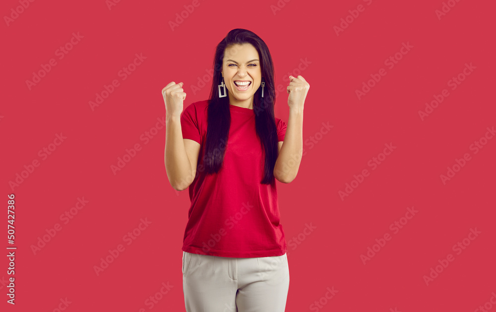 Joyful excited woman clenching her fists rejoicing in her victory or success on red background. Happy caucasian woman laughing shouting yes and happily clenching fists looking at camera. Banner. Joyful excited woman clenching her fists rejoicing in her victory or success on red background. Happy caucasian woman laughing shouting yes and happily clenching fists looking at camera. Banner.