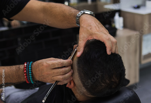 Hands of barber shaving a client with a straight razor