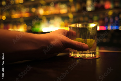 Hand with a cocktail on bar counter in a restaurant, pub. Fresh drink. Jin glass. Alcoholic cooler beverage at nightclub or bar on colorful lightbackground.