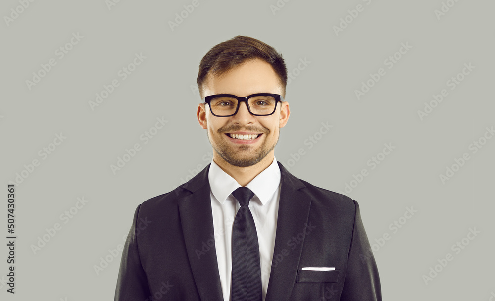 Headshot portrait of smiling young businessman in suit and glasses posing isolated on grey studio background. Profile picture of happy male entrepreneur or manager. Recruitment. Headshot portrait of smiling young businessman in suit and glasses posing isolated on grey studio background. Profile picture of happy male entrepreneur or manager. Recruitment.