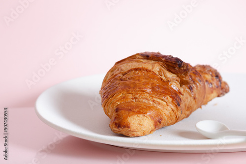 Croissant on white plate on pink background.