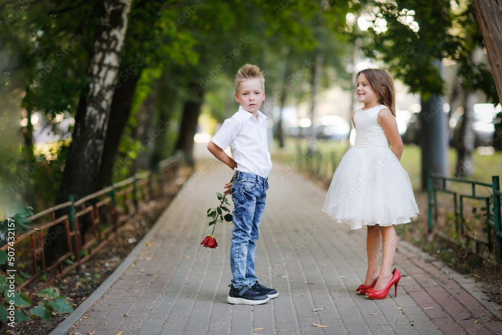 cute couple of children boy and girl, boy gives his girlfriend rose for walk in summer. Girl child in high heels, children play dating and courtship, relationship and growing up concept cute couple of children boy and girl, boy gives his girlfriend rose for walk in summer. Girl child in high heels, children play dating and courtship, relationship and growing up concept