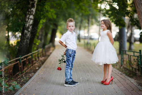 cute couple of children boy and girl, boy gives his girlfriend rose for walk in summer. Girl child in high heels, children play dating and courtship, relationship and growing up concept