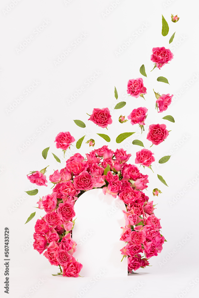 Fresh pink roses as framing of arch with green leaves and buds fly as swirl on abstract white scene mockup for presentation cosmetic products, goods, vertical. Summer template for advertising, design.