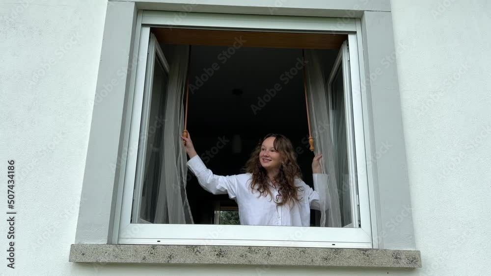 Window She a teenage girl splits the white curtains and looks out the white window ...