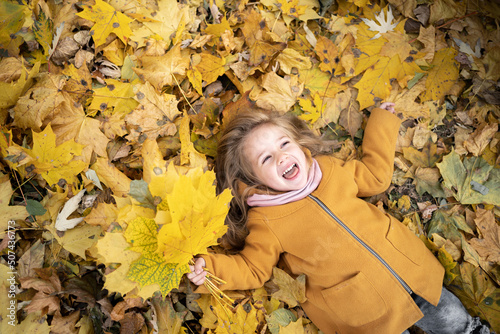 Happy child walking in autumn park. Little funny girl lies on yellow leaves in the forest. Preschooler outdoors. autumn nature vacation