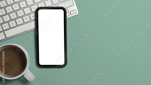 Flat lay smart phone, coffee cup and keyoard on green background. Copy space, blank screen for advertise text photo