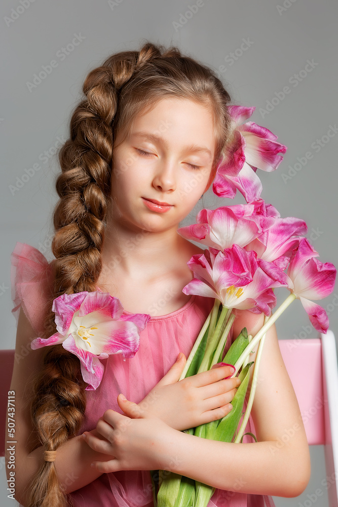 Close portrait of a girl with long hair with an orchid flower on a gray background