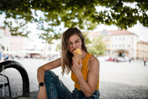 Happy young woman is making funny faces while posing with gelato ice cream on a beautiful sunny summer day