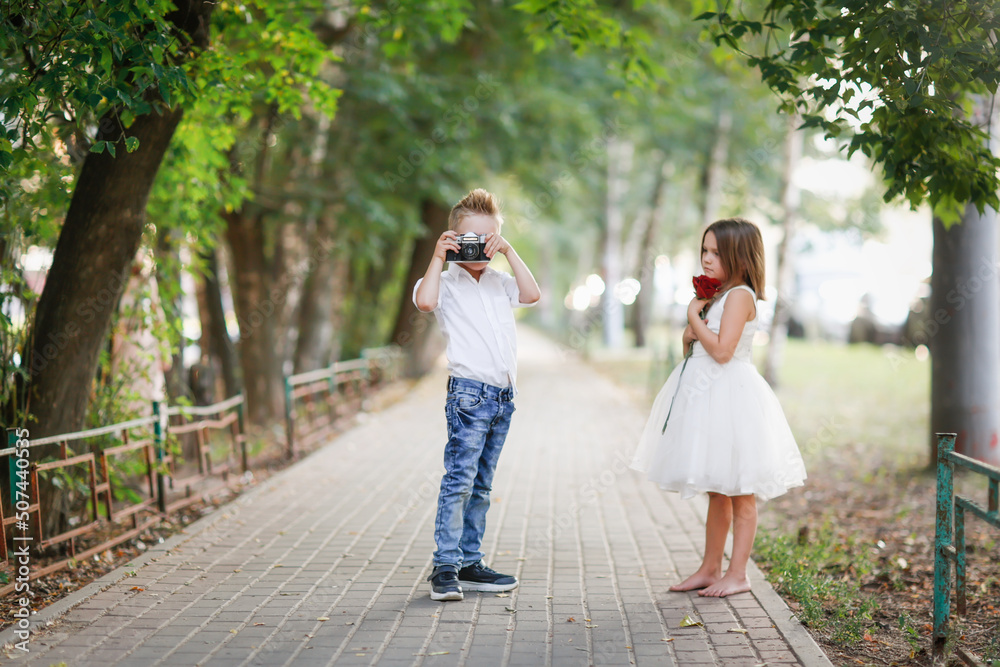 Funny romantic couple kids. boy with retro film camera photographs girl with rose, summer walks in park.