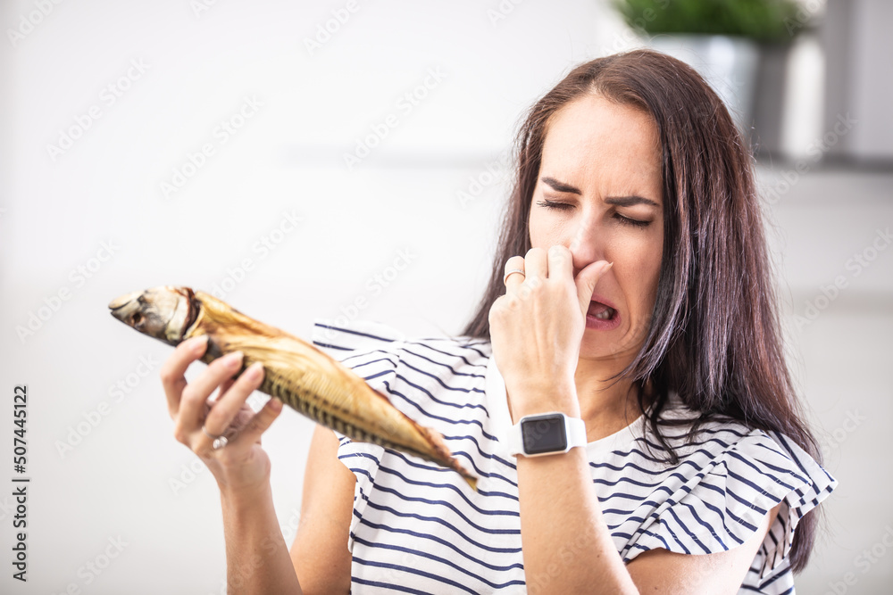 Woman holds stinky fish holds her nose with disgusted facial expression from the smell - obrazy, fototapety, plakaty 