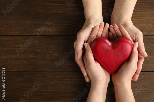 Young and elderly women holding red heart at wooden table  top view. Space for text