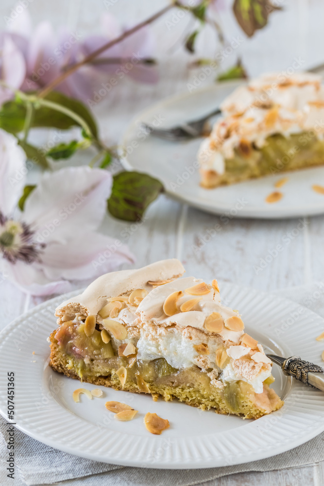 Pieces of rhubarb pie with meringue topping and roasted almonds on white wooden background