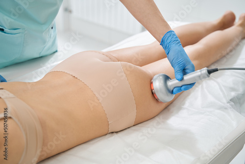 Beautician performing radiofrequency therapy against saggy thigh skin