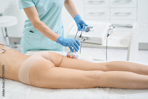 Cosmetologist refreshing and tightening leg skin with radio wave lifting
