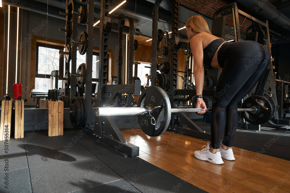 Strong athletic lady performing deadlift exercise indoors