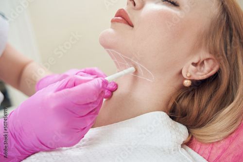 Doctor hands in pink gloves is making marks on client chin in beauty center