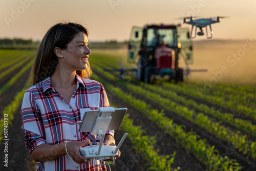 Farmer woman driving drone in field with tractor in background photo