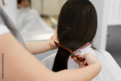 Strong, shiny and healthy long brunette hair. Hairdresser combing the hair of the client. Close-up of beautiful silky hair is in hands of stylist