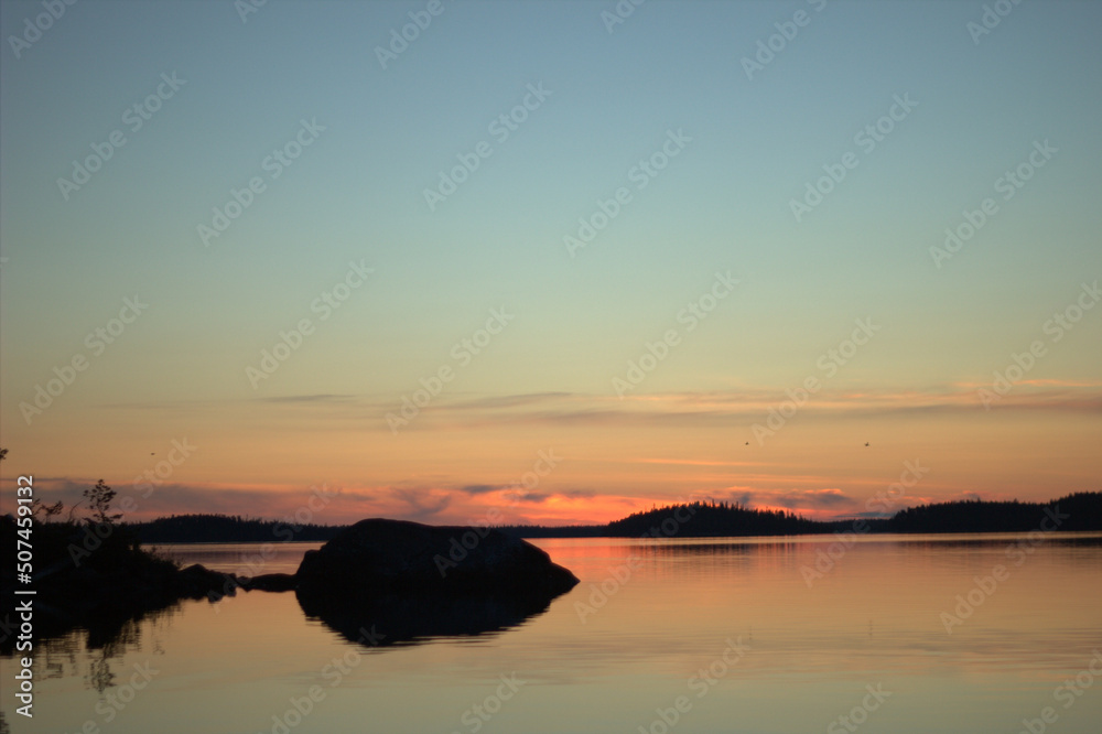 A lovely island in the middle of the northern lake during the sunset. Three swans on a horizon are heading North. A lovely island in the middle of the northern lake during the sunset. Three swans on a horizon are heading North.