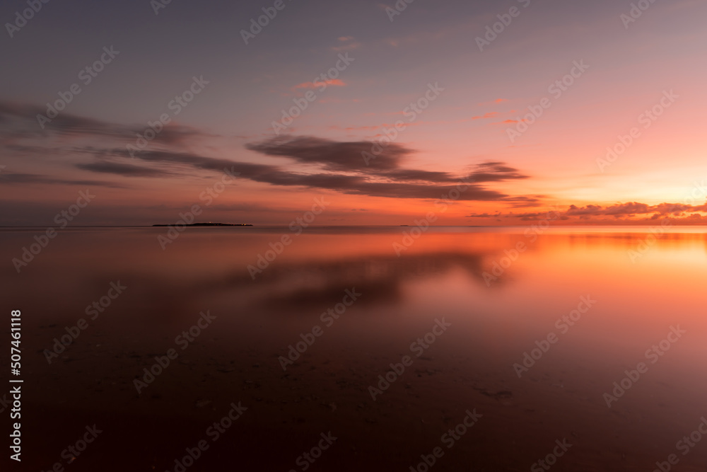 Amazing dawn at seashore, colorful sky reflecting on the sea, island on background.