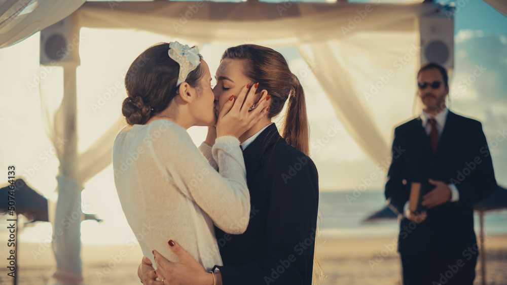 Fototapeta premium Close Up of Female Queer Couple Exchange Rings and Kiss at Outdoors Wedding Ceremony Near Sea. Happy Two Lesbian Women in Love Say Their Vows and Get Married. LGBTQ Relationship Goals.