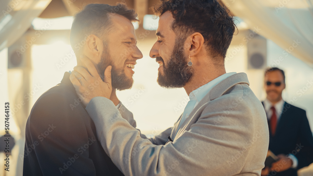 Close Up of Handsome Gay Couple Exchange Rings and Kiss at Outdoors Wedding Ceremony Venue Near the Sea. Two Happy Men in Love Share Their Vows and Get Married. LGBTQ Relationship Goals.