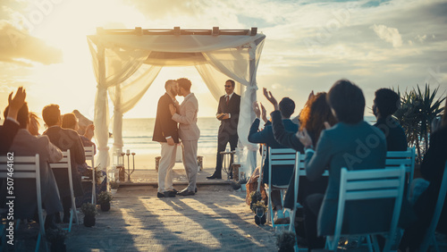 Handsome Gay Couple Exchange Rings and Kiss at Outdoors Wedding Ceremony Venue Near the Sea. Two Happy Men in Love Share Their Big Day with Diverse Multiethnic Friends. LGBTQ Relationship Goals.