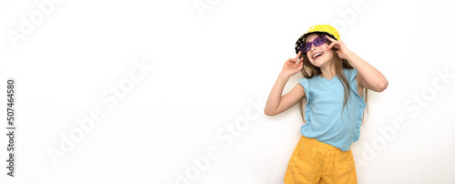 a beautiful little girl in a blue T-shirt, sunglasses and a sun hat on a gray flat background, children's emotions, a place for text, a girl with glasses in a purple frame smiling happily.