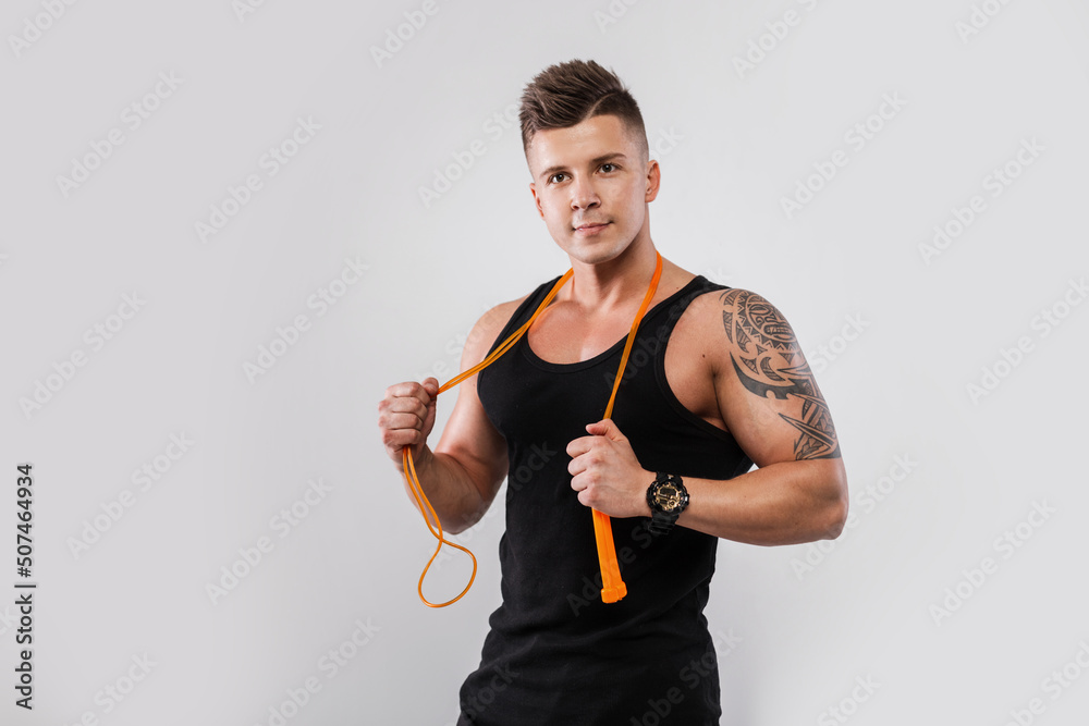 Handsome fitness man model with hairstyle in a sports black tank top with a jump rope on a white background in the studio Handsome fitness man model with hairstyle in a sports black tank top with a jump rope on a white background in the studio