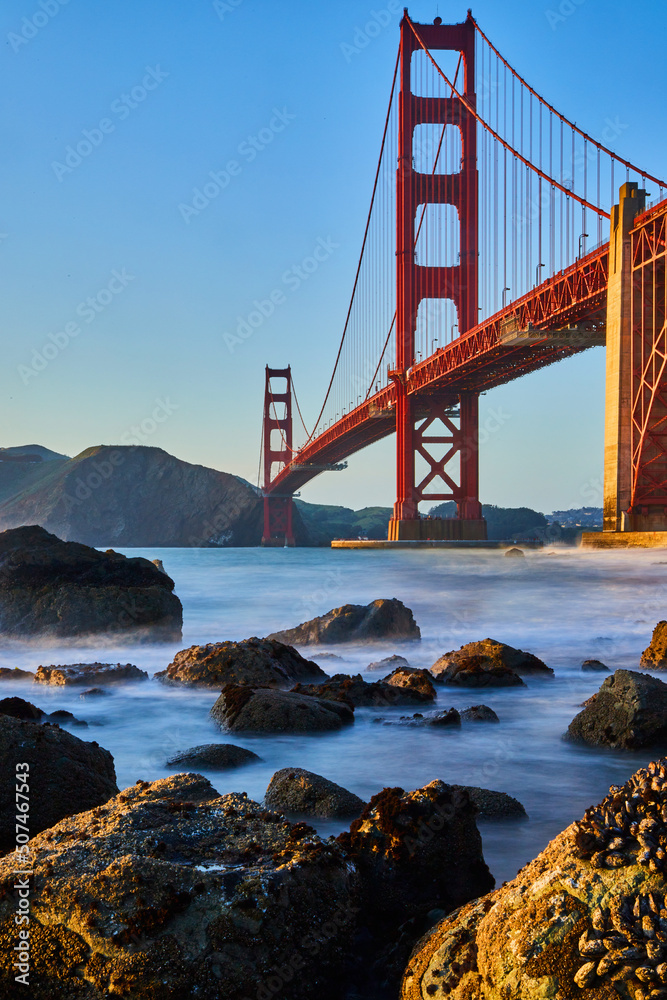 Beach rocks covered in mussels by Golden Gate Bridge at sunset