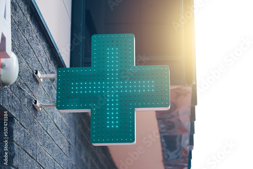 Pharmacy green light cross board. Drugstore signboard on building. Store decoration of downtown. Logo of city dispensary.